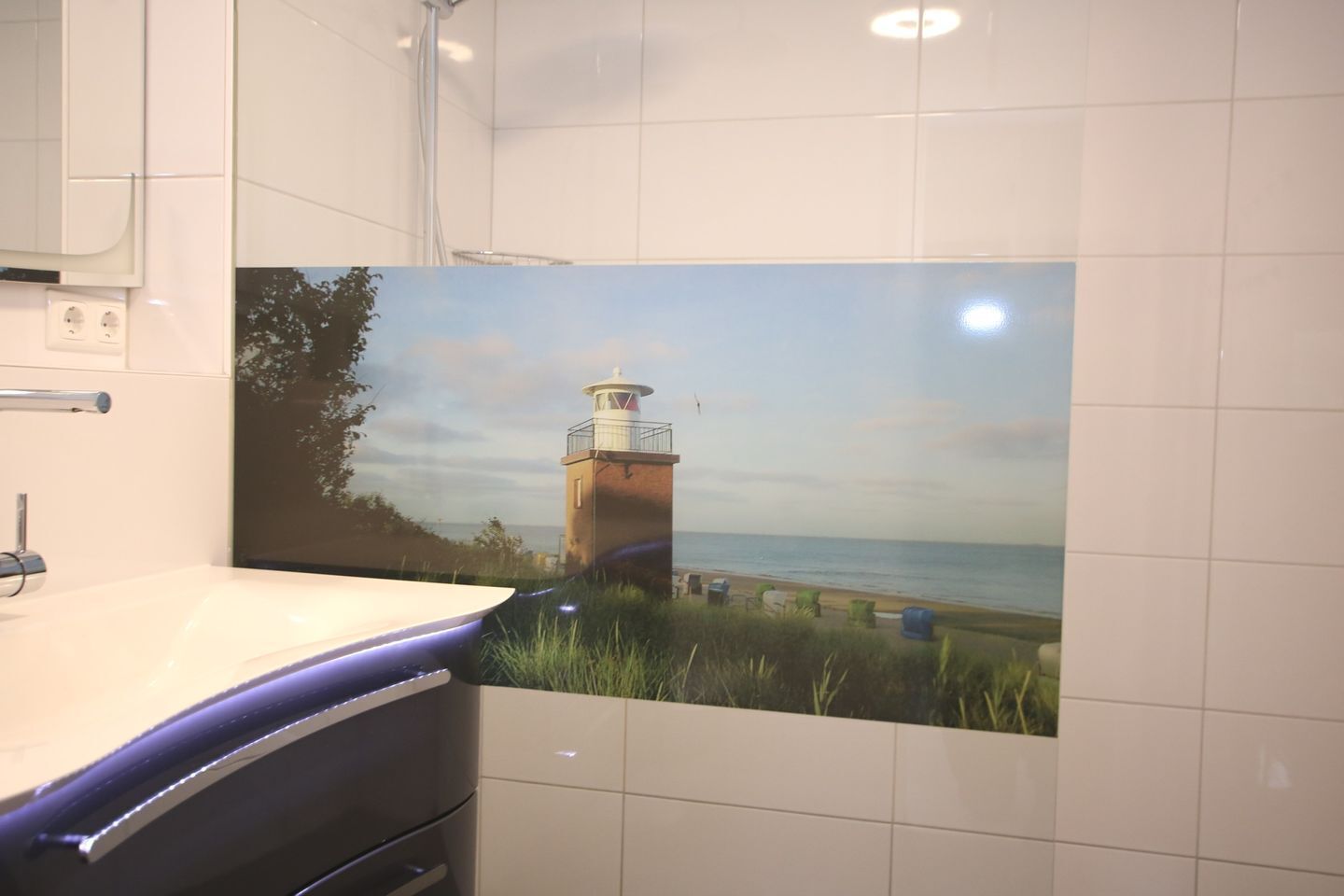 A bathroom with a large wall decal of a lighthouse by the sea, a white sink, and a mirror.