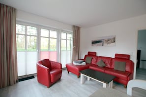 Un salon moderne avec un canapé en cuir rouge, un fauteuil assorti et une table basse. De grandes fenêtres laissent entrer la lumière naturelle et offrent une vue sur la verdure environnante.