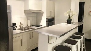 Eine moderne Küche mit weißen Schränken, einer zentralen Kochinsel mit Barhocker, einem Einbauofen und einer Kaffeemaschine.