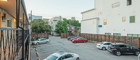 A parking lot with several cars, a building with a white facade, and a fence.