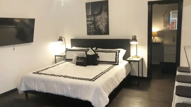 Ein Schlafzimmer mit einem Bett, zwei Nachttischlampen, einem Deckenventilator, einem Flachbildfernseher und einem Wandbild.