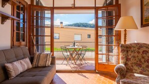 Un balcón abierto con un sofá, un sillón floral y una mesa con asientos exteriores.