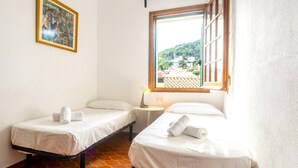 Una habitación con dos camas individuales, una mesita con lámpara, una ventana con vistas a una colina y un cuadro en la pared.