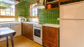Una cocina con baldosas verdes, armarios de madera, microondas, estufa y pileta.
