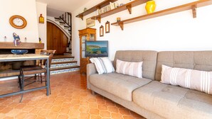 Una sala de estar acogedora con un sofá, una mesa de comedor con sillas, una escalera y un televisor en la pared.