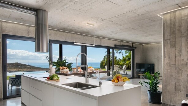 A modern kitchen with a large island, a sink, and a view of the ocean. - KARAT Villa Atelier de la Vega (Playa Paraiso)