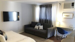 A hotel room with a bed, a sofa, a desk, a chair, a TV, and a window with curtains. - Montrose Stylish Studio! Medical Center 45 (Houston)