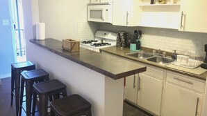A kitchen with white cabinets, a microwave, a gas stove, and a sink. There are three stools at the counter. - Montrose Stylish Studio! Medical Center 45 (Houston)