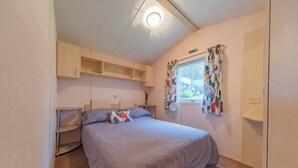 Un dormitorio con cama, estantes empotrados, una ventana con cortinas e iluminación en el techo.