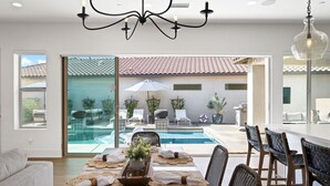 A dining area with a pool view, a chandelier, and a bar area. - Desert pool retreat w/ mountain views (La Quinta)