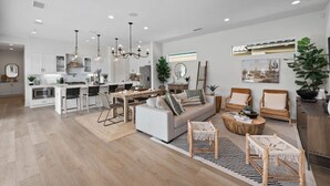 A spacious living area with a sofa, coffee table, and seating area. There is a kitchen in the background with white cabinets and a dining area with a table and chairs. - Desert pool retreat w/ mountain views (La Quinta)