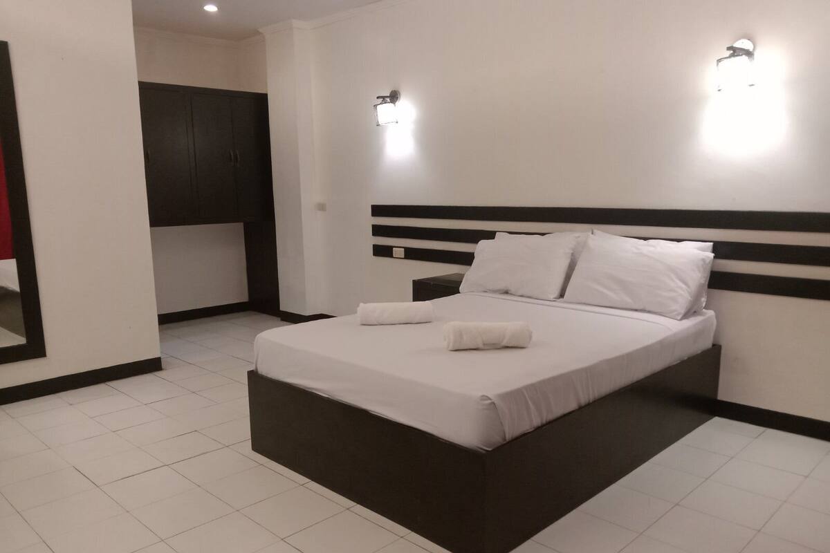 Habitación de hotel moderna con una cama grande, dos mesitas de noche, un armario y una pequeña zona de kitchenette.