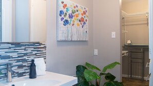 A bathroom with a tiled backsplash, a sink, a mirror, a potted plant, and a colorful floral painting on the wall. - Montrose Stylish Studio! Medical Center 46 (Houston)