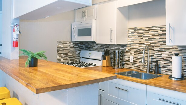 A modern kitchen with a wooden countertop, stainless steel sink, white cabinets, a microwave, and a gas stove. - Montrose Stylish Studio! Medical Center 46 (Houston)