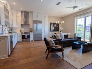 A modern kitchen with white cabinets, stainless steel appliances, and a dining area with a dark sofa and a small table.