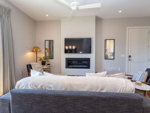 A modern bedroom with a bed, a TV, a fireplace, and a ceiling fan.