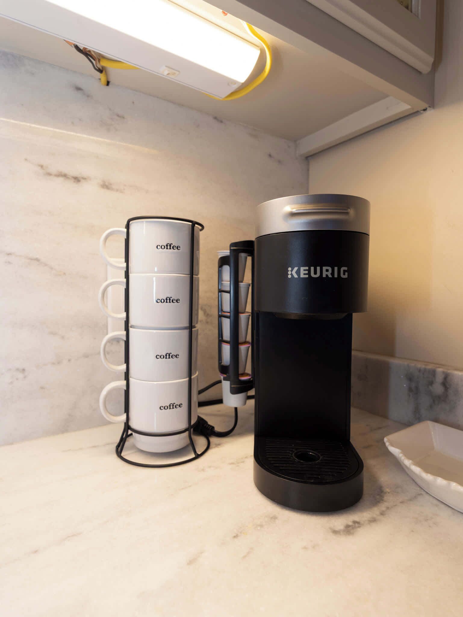 A Keurig coffee maker and a coffee mug holder with multiple mugs on a marble countertop.