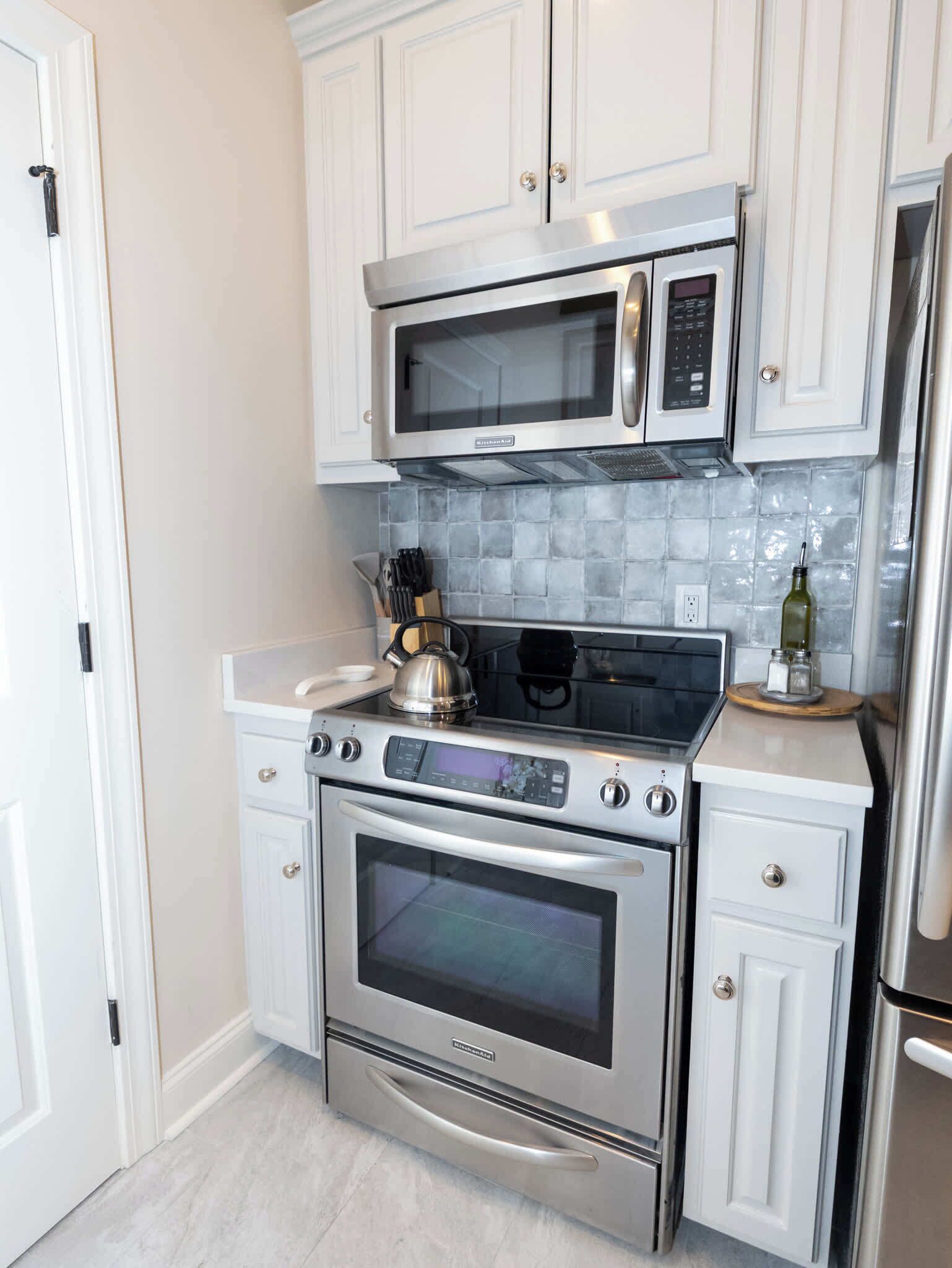 A kitchen with white cabinets, a stainless steel oven, a microwave, and a tiled backsplash.