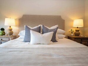 A neatly made bed with patterned bedding, two bedside tables with lamps, and a decorative vase on one table.