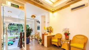 A hotel reception area with wicker furniture, a reception desk, and a view of the street outside. - Spring House Hotel (Ho Chi Minh City)