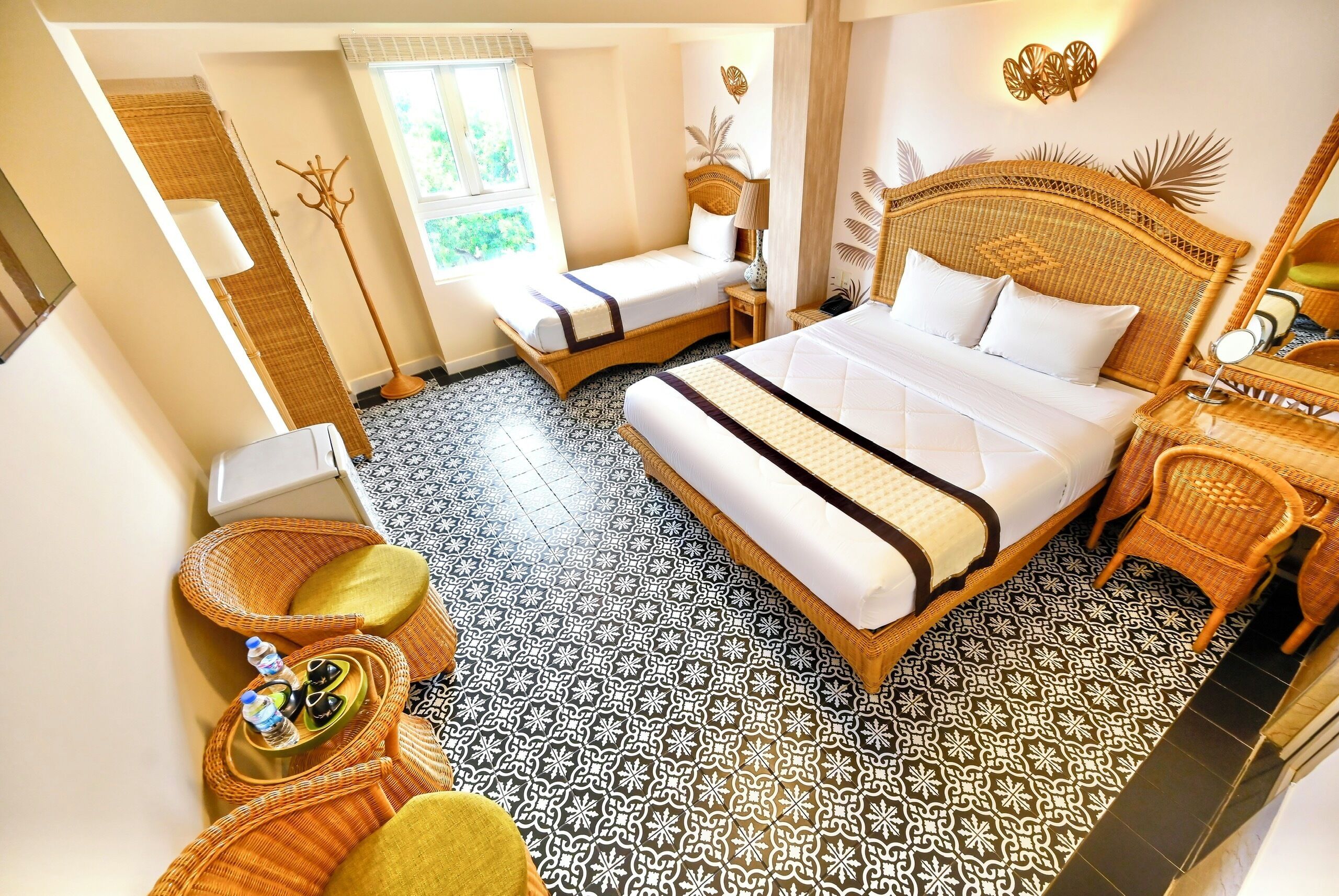 A hotel room with a large bed, a smaller sitting area, a window with a view, a floor lamp, and a mirror.
