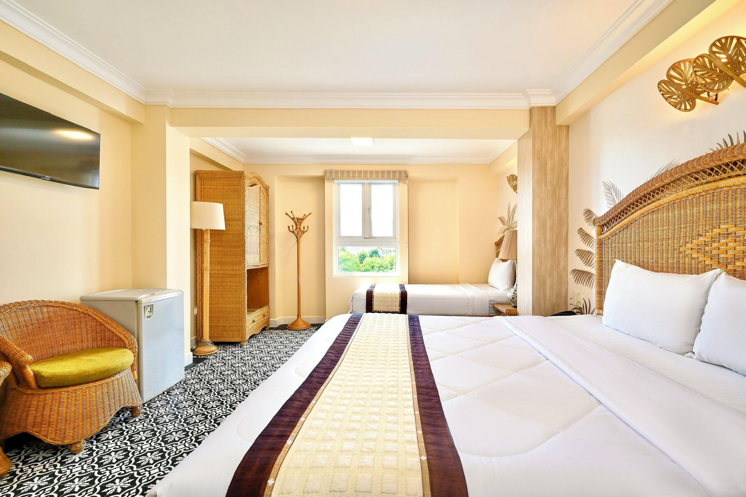 A hotel room with a large bed, a small desk, a chair, a television, and a window with a view of greenery.