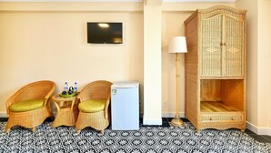 A room with two wicker chairs, a small table with bottles, a white refrigerator, a television on the wall, and a large wicker wardrobe. - Spring House Hotel (Ho Chi Minh City)