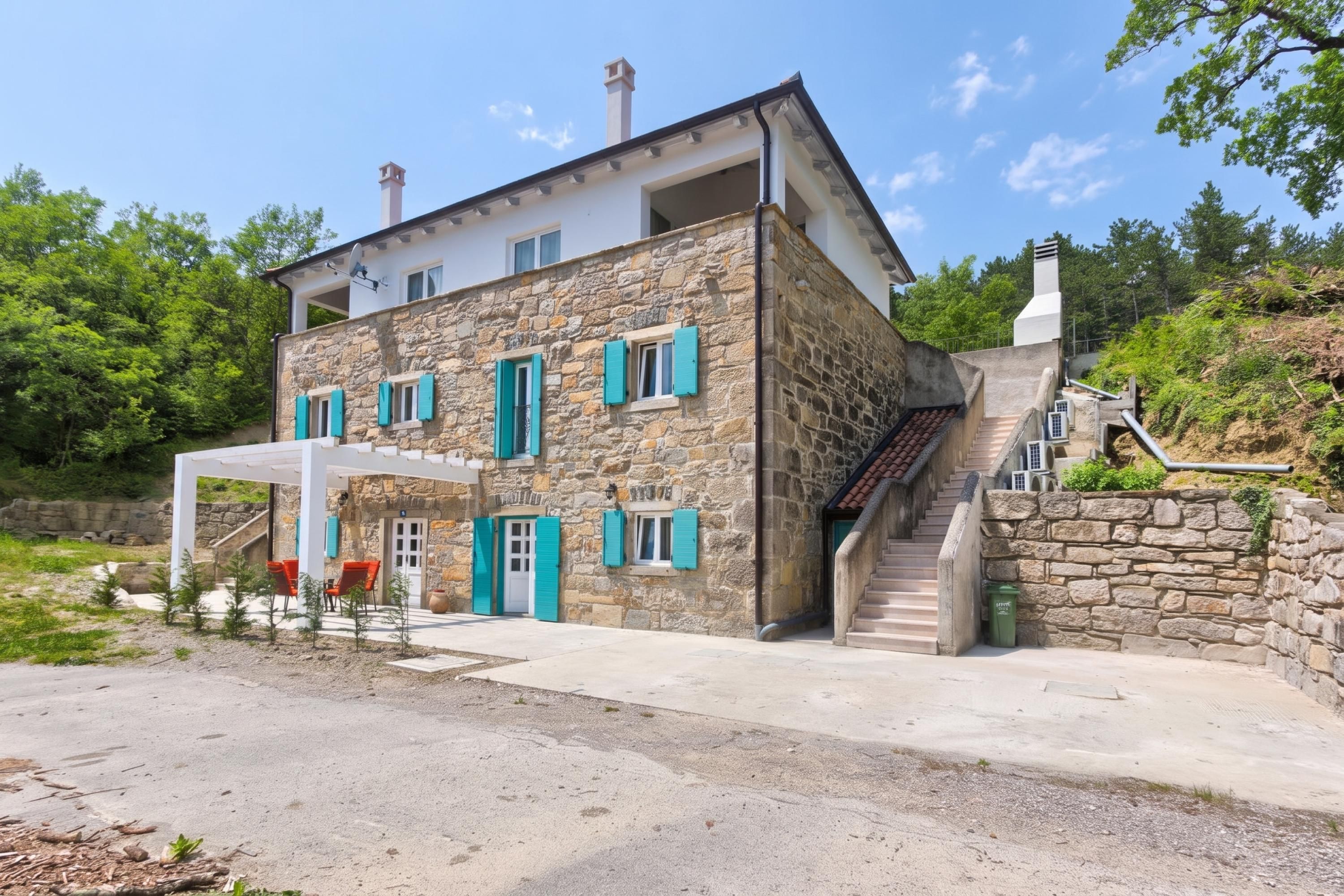 Une maison en pierre à deux étages, dotée d’un patio couvert et d’un escalier menant à l’étage supérieur.