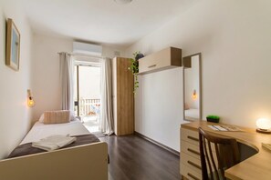 A bedroom with a bed, a desk, a chair, a dresser, a mirror, and a potted plant.