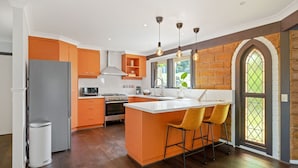 Een moderne keuken met oranje kastjes, een centraal eiland met barstoelen, een fornuis en een groot raam met uitzicht op groen.