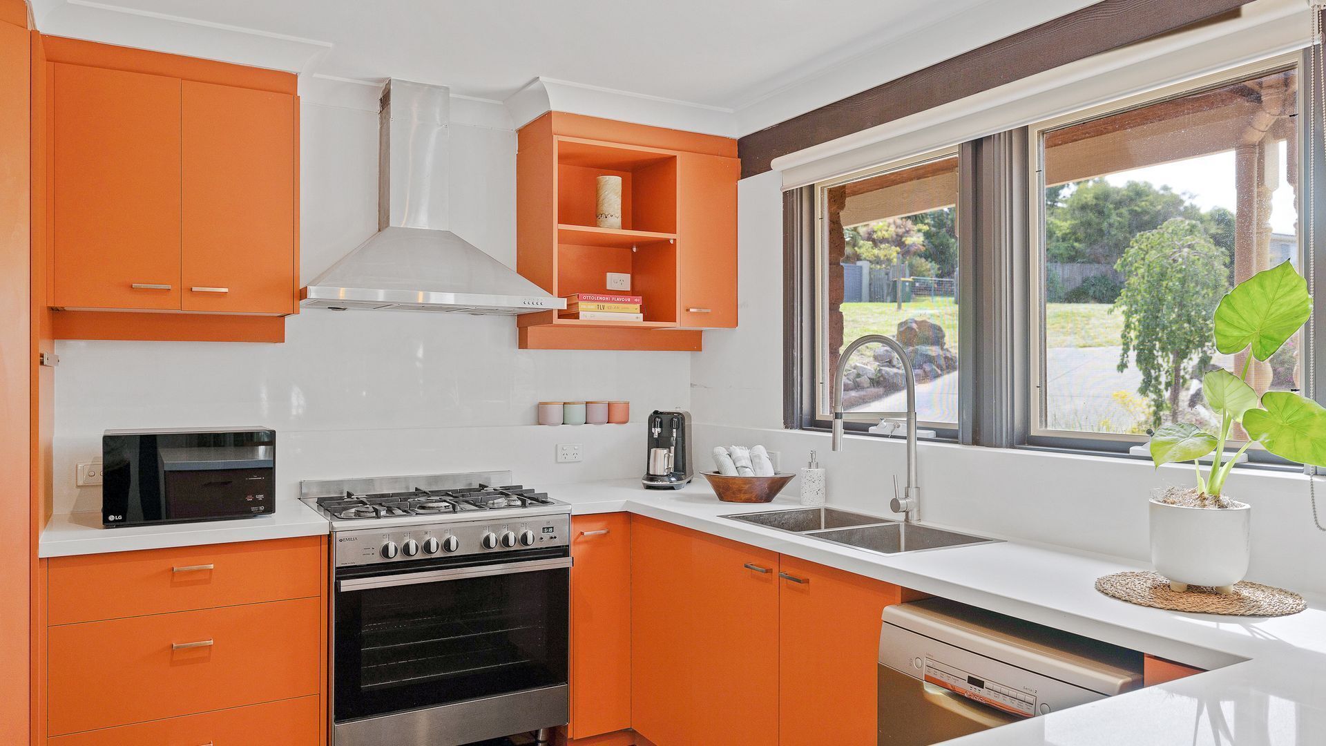 Une cuisine moderne avec des meubles de couleur orange, une cuisinière à gaz, un four encastré et une fenêtre donnant sur l’extérieur.