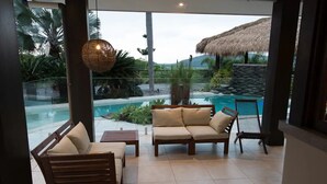 A modern indoor seating area with a pool view, featuring a sofa, chairs, and a hanging light fixture.