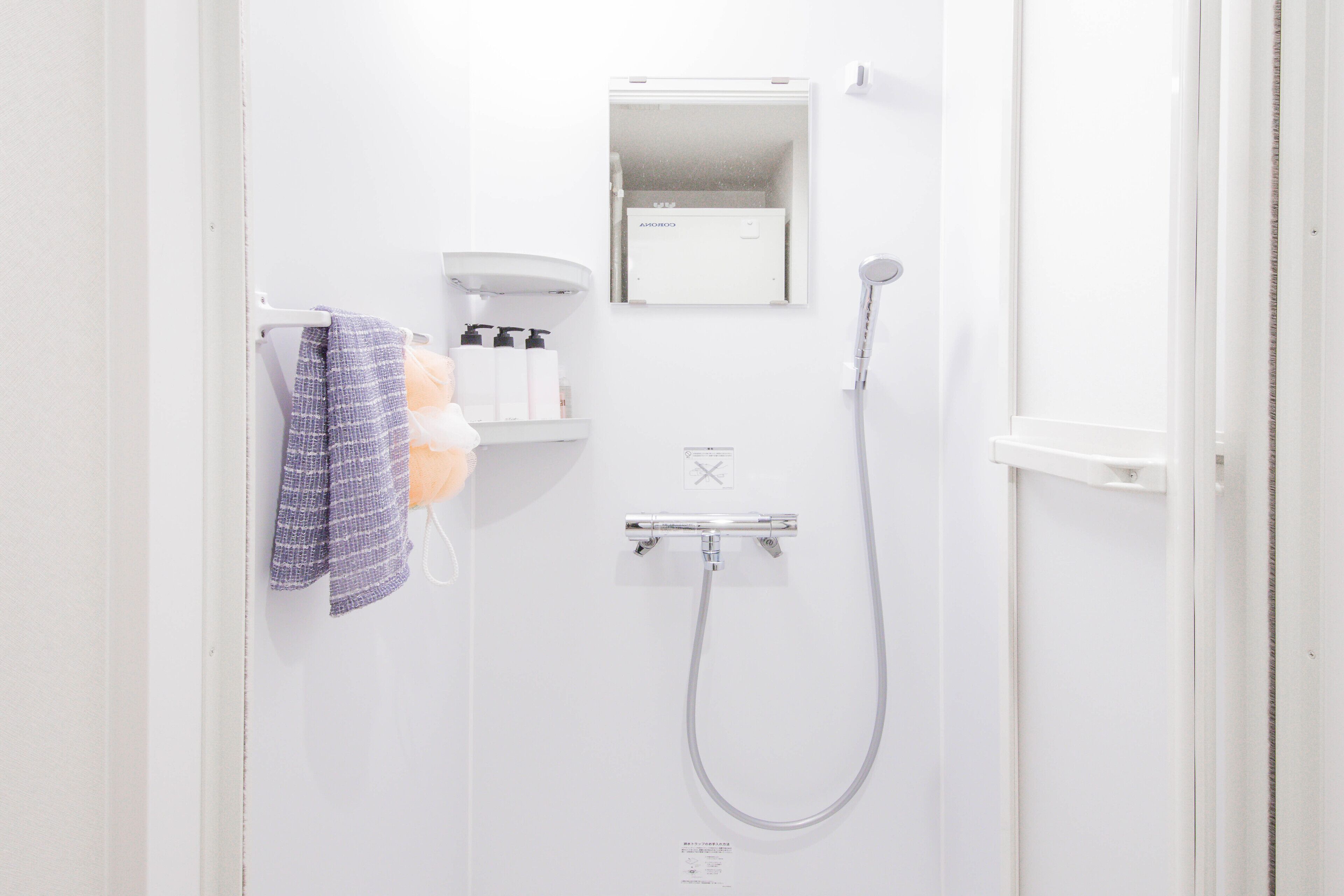 A white bathroom with a shower, a towel rack with a towel, and a shelf with toiletries.