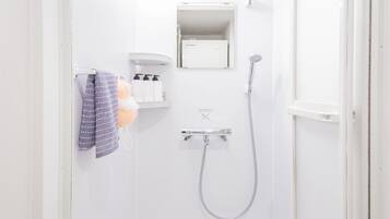 A white bathroom with a shower, a towel rack with a towel, and a shelf with toiletries.