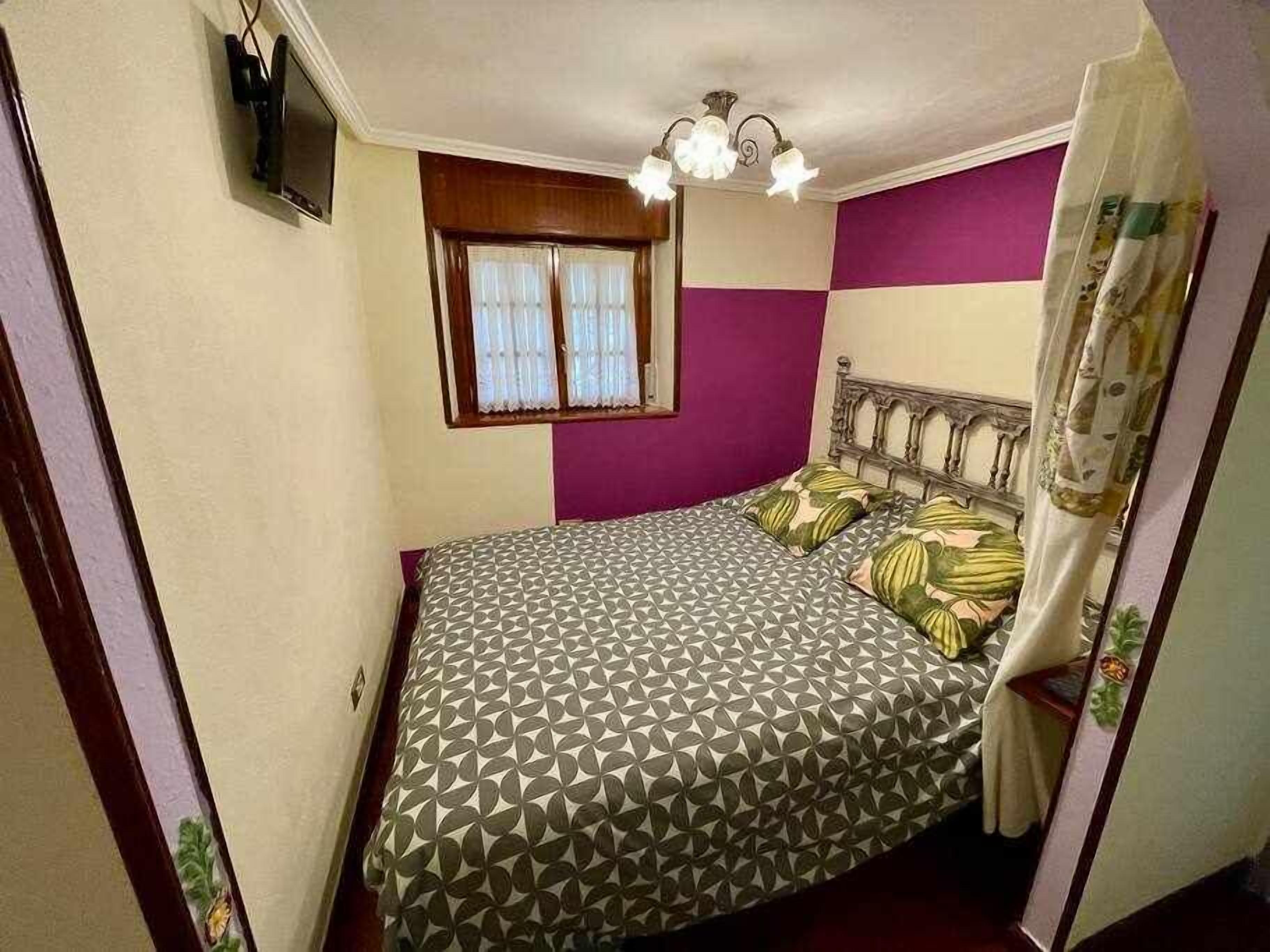 Ein Schlafzimmer mit einem Bett, einem fensterbelaubten Fenster, einer Deckenleuchte und einer Wand in Lila und Weiß.