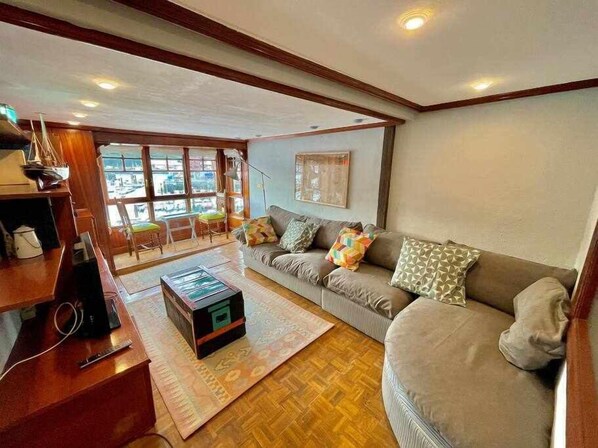 A cozy living room with a sofa, a coffee table, and a wooden floor. There are windows providing natural light and a view of the outside. - Utsa Eski -piso con Encanto en 1ª Linea de Puerto (Bermeo)
