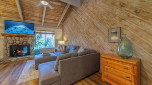 A cozy living room with a stone fireplace, a flat-screen TV, a sofa, and a wooden dresser. - Remodeled Condo w/ View & Near Gondola 590 (Mammoth Lakes)