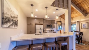 A modern kitchen with a large island, bar stools, pendant lighting, and a view of the dining area. - Remodeled Condo w/ View & Near Gondola 590 (Mammoth Lakes)