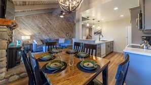 A dining area with a wooden table set for four, surrounded by chairs. A stone fireplace is visible to the left. - Remodeled Condo w/ View & Near Gondola 590 (Mammoth Lakes)