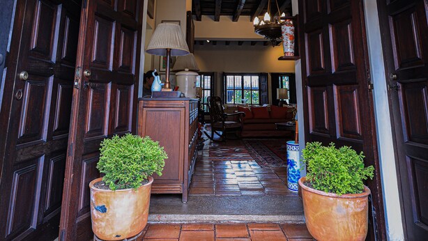 A hallway with wooden doors, a chandelier, and potted plants. - Hotel Casa Bansley (Antigua Guatemala)