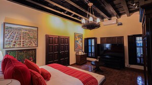 A hotel room with a large bed, a TV, wooden cabinets, and artwork on the walls. - Hotel Casa Bansley (Antigua Guatemala)