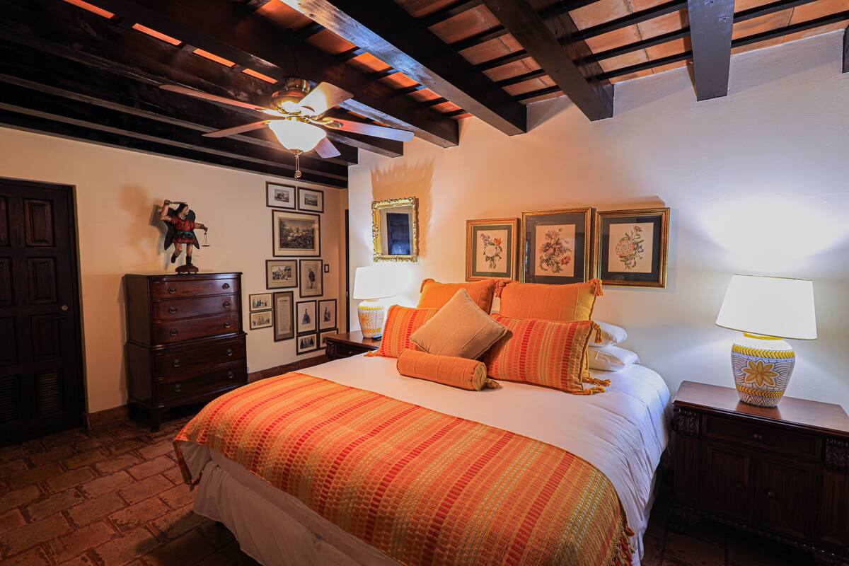 Un dormitorio con una cama grande, vigas de madera en el techo, un aparador y cuadros enmarcados en la pared.