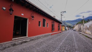 A cobblestone street lined with red buildings, a clear sky, and distant mountains. - Hotel Casa Bansley (Antigua Guatemala)