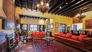 A spacious living room with a large red sofa, a wooden coffee table, and a patterned rug. There are multiple chairs and a fireplace. - Hotel Casa Bansley (Antigua Guatemala)
