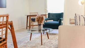 Un salon avec une table basse en verre, un canapé bleu, un fauteuil en osier et une petite table sur laquelle est posé un vase.
