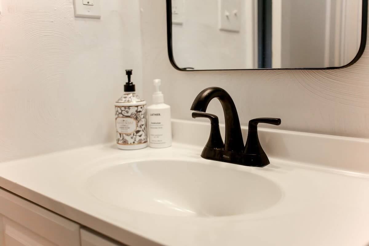 A bathroom sink with a black faucet, a white soap dispenser, and a decorative container.