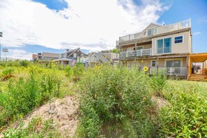 A coastal residential area with multi-story houses, sandy terrain, and a clear sky.