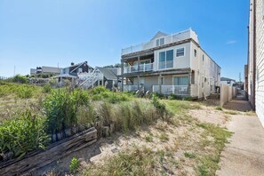 Um imóvel à beira-mar com uma casa de dois andares, um alpendre coberto e uma área arenosa com vegetação.