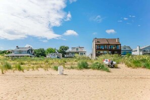 Uma praia com casas ao fundo, um caminho de areia e um barco na areia.
