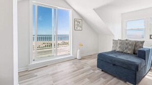 Ein Zimmer mit Balkon, einer Couch, einer Vase mit Blumen und einem gerahmten Bild an der Wand.